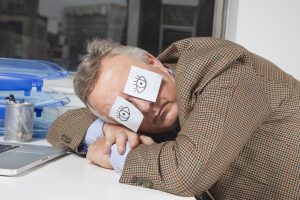 Businessman sleeping with sticky notes on eyes at desk in office